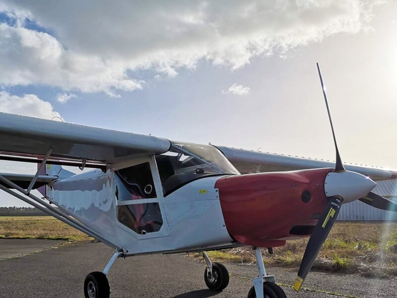 Petit avion blanc et rouge stationné sur la piste d'un aérodrome sous un ciel partiellement nuageux.