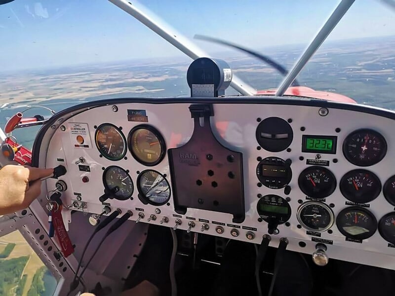 Tableau de bord d'un avion léger avec plusieurs instruments de vol et une main sur le levier de commande.