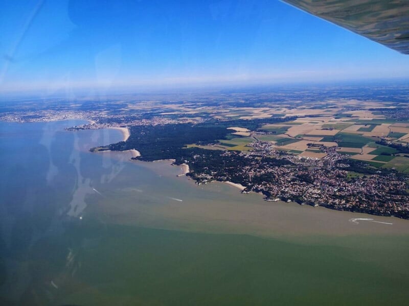 Vue aérienne d'une côte avec des terres agricoles et une ville au bord d'une étendue d'eau.
