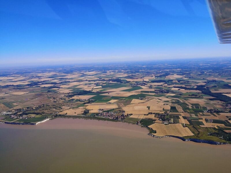 Vue aérienne d'une campagne avec champs cultivés et une étendue d'eau au premier plan.