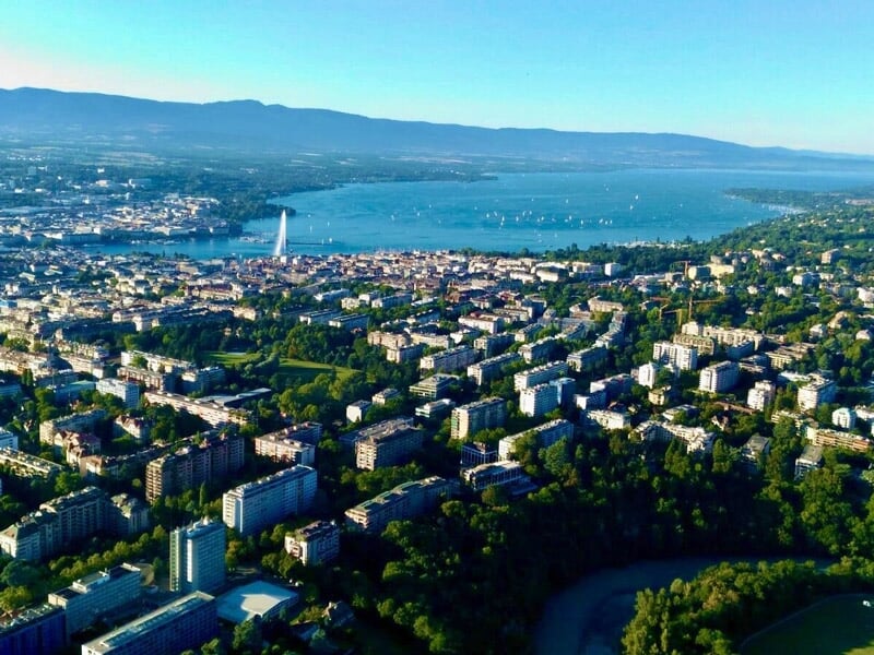 Vue aérienne de Genève avec le lac Léman et les montagnes en arrière-plan sous un ciel clair.