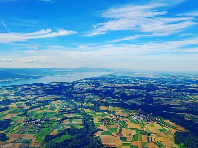 Paysage rural avec champs et collines verdoyantes vus depuis une montgolfière en vol.