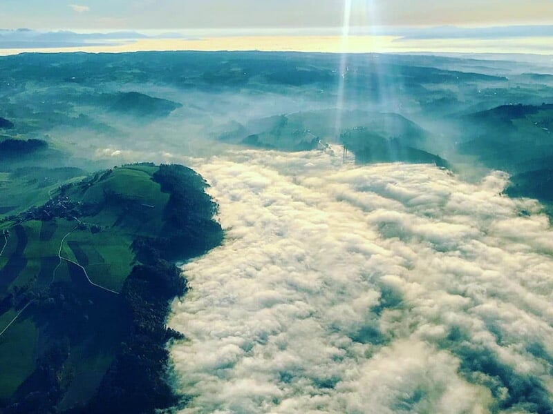 Vue aérienne d'une vallée couverte de nuages avec des collines verdoyantes autour.