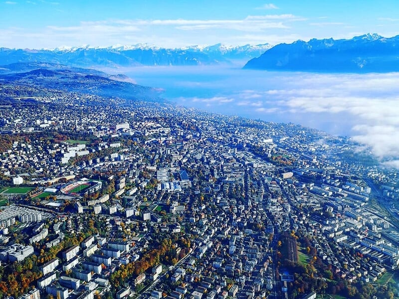 Vue panoramique de Lausanne avec la ville, le lac Léman et les montagnes enneigées au loin.