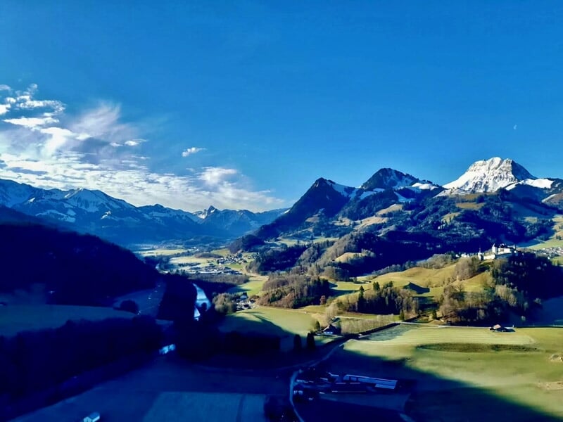 Paysage montagneux avec des sommets enneigés et des vallées verdoyantes au lever du soleil.