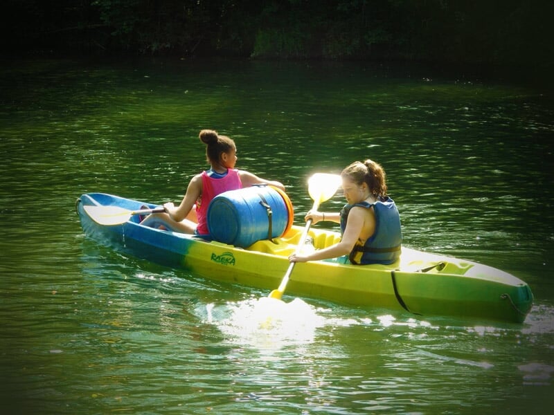 Deux personnes pagayant dans un kayak jaune et bleu sur une rivière paisible avec des gilets de sauvetage.