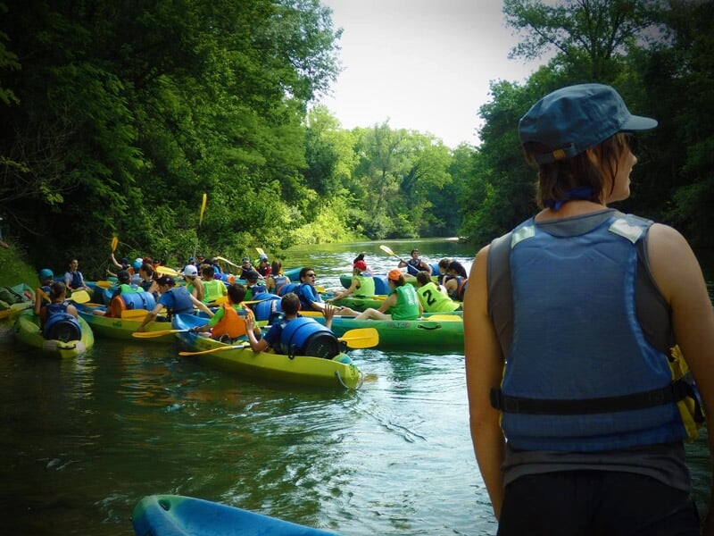 Groupe de personnes en kayak sur une rivière entourée de végétation dense, vues depuis l'arrière d'un observateur.