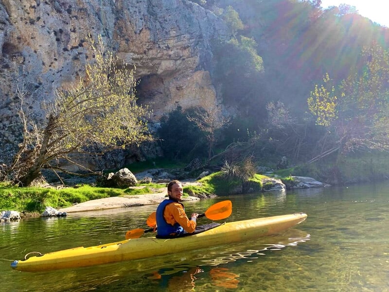 Homme pagayant seul dans un kayak jaune sur une rivière avec une falaise rocheuse en arrière-plan.