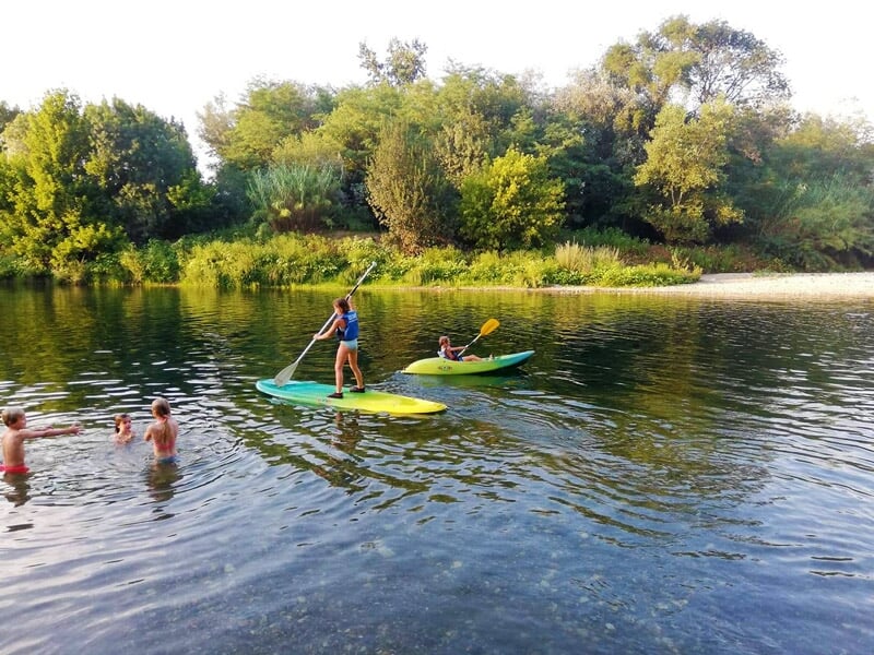 Deux personnes pagayant sur des planches de stand-up paddle sur une rivière au coucher du soleil avec d'autres baigneurs.