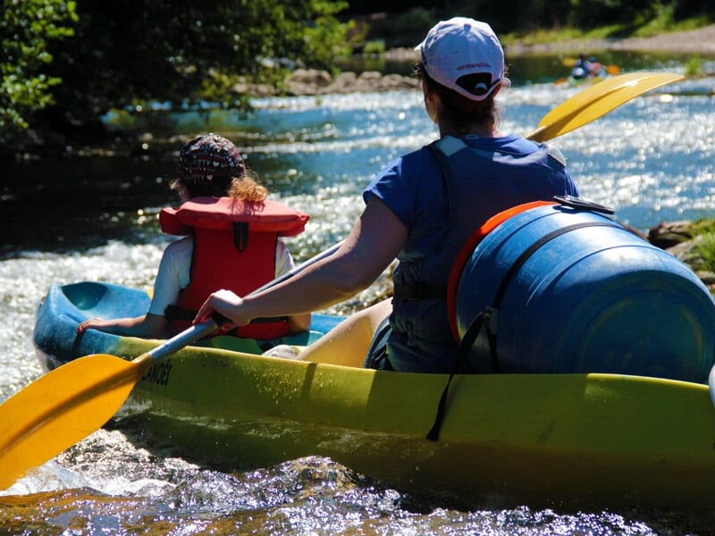 Deux personnes pagayant dans un kayak jaune sur une rivière avec des rapides et une végétation dense autour.