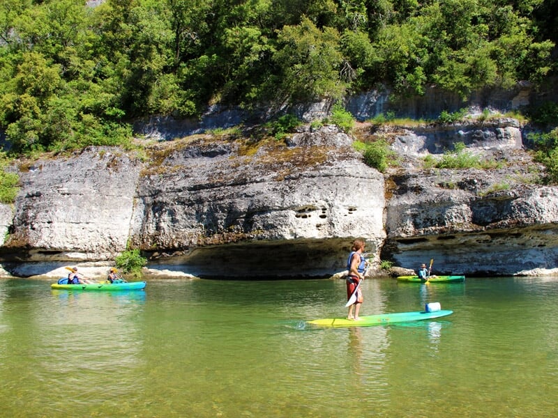 Deux personnes pagayant dans un kayak bleu et vert sur une rivière calme entourée d'arbres verts.