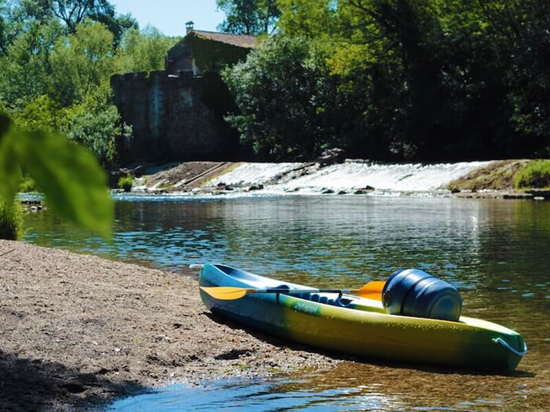 Personne debout sur une planche de stand-up paddle pagayant sur une rivière calme avec des falaises rocheuses.