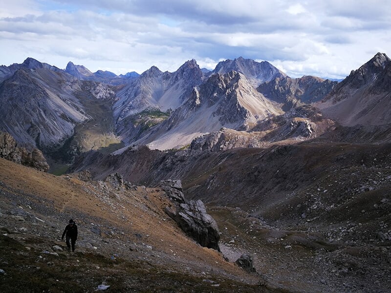 Un randonneur marche seul sur un chemin de montagne avec des pics escarpés en arrière plan