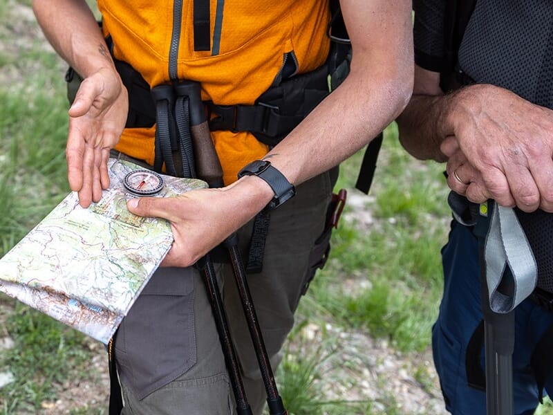 Un accompagnateur en montagne explique à un randonneur comment s'orienter avec une carte et une boussole