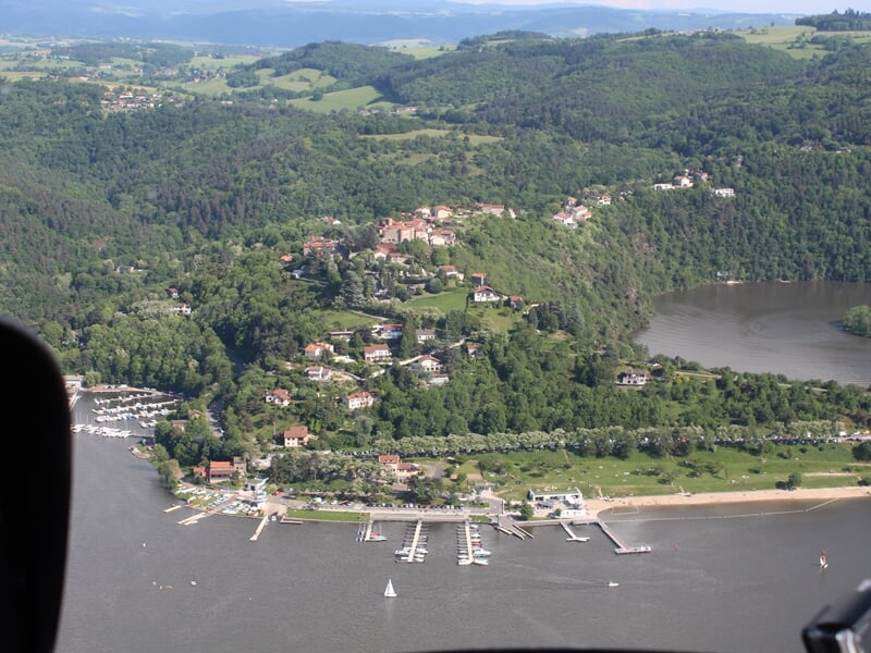 Vue aérienne d'un village au bord d'un lac avec des bateaux amarrés et une forêt dense.