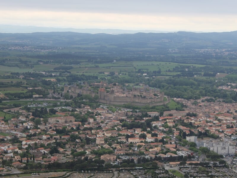 Vue aérienne d'une ville fortifiée avec remparts et toits rouges sous un ciel clair.