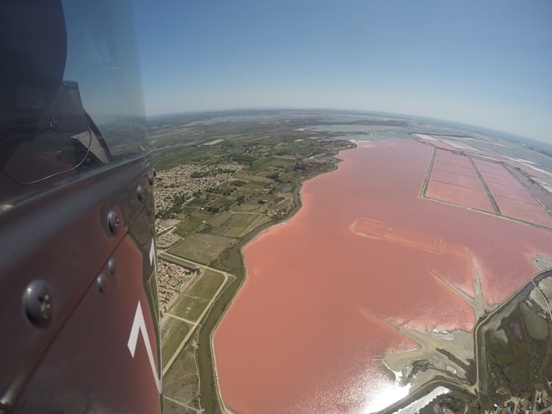 Étendue d'eau rose salée vue depuis un hélicoptère avec zones agricoles et ciel bleu.