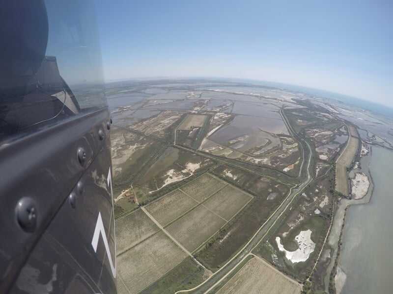 Paysage de marais salants et canaux vus du ciel avec un hélicoptère en vol au premier plan.