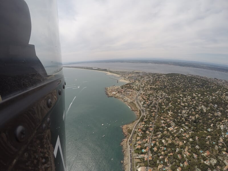 Vue aérienne d'une côte avec maisons, plages et mer calme sous un ciel partiellement nuageux.