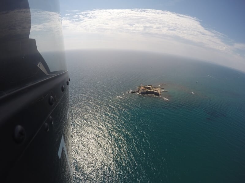 Île rocheuse entourée d'eau scintillante vue depuis un hélicoptère en plein vol.