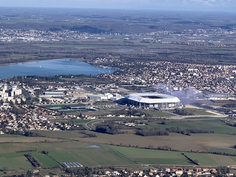 Vue aérienne d'un stade et d'une ville avec plans d'eau et collines en arrière-plan.
