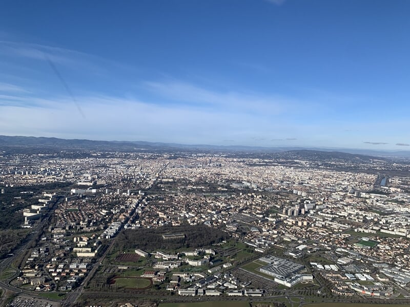 Vue étendue d'une ville avec toits, routes et collines lointaines sous un ciel bleu.