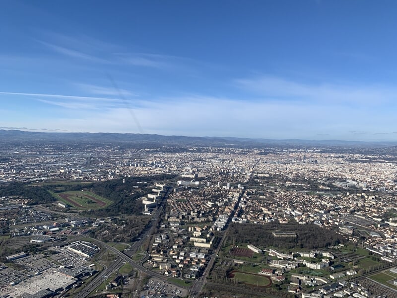 Vue aérienne d'une grande ville avec quartiers résidentiels et zones vertes visibles.