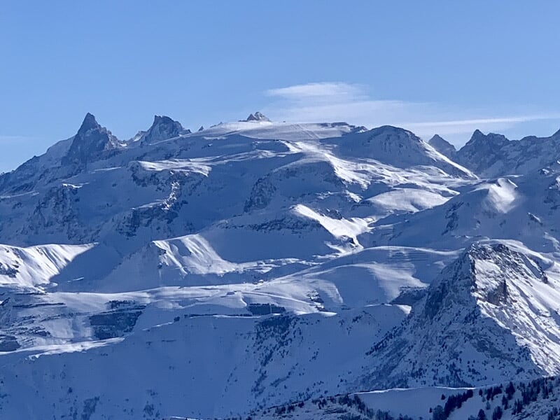 Vue aérienne d'une ville entourée de montagnes enneigées sous un ciel bleu limpide.