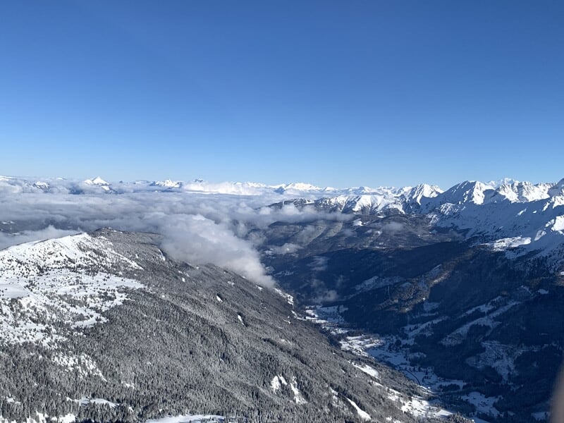 Vue étendue d'une ville avec toits, routes et montagnes enneigées au loin, lors d'un baptême en hélicoptère près du Vercors.