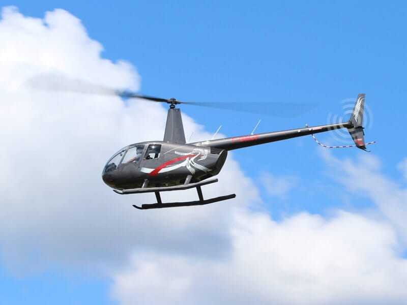 un hélicoptère R44 vole avec des nuages blancs en arrière plan