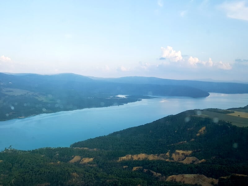 Paysage montagneux enneigé avec un lac au fond de la vallée sous un ciel bleu, lors d'un vol en hélicoptère près des gorges du Verdon.