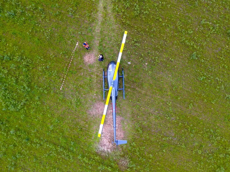 Vue aérienne d'un hélicoptère posé sur un terrain herbeux avec deux personnes à proximité, à l'aérodrome de Muret-Lherm.