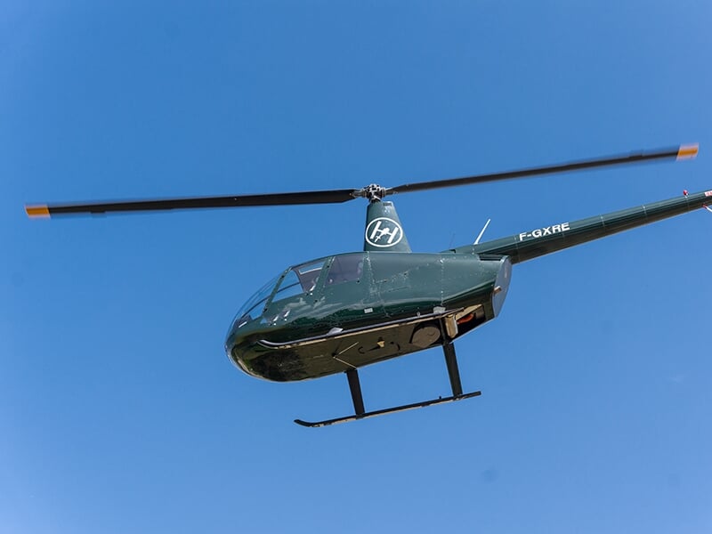 Hélicoptère noir et vert vu de dessous, volant dans un ciel parfaitement dégagé.