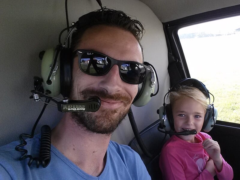 Un pilote souriant avec un jeune passager portant des casques audio à bord d’un hélicoptère.