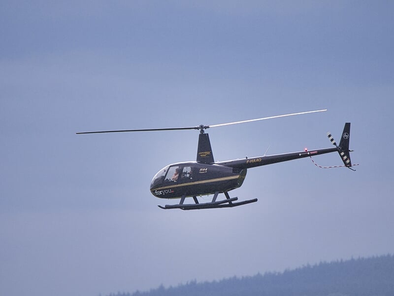 Hélicoptère en plein vol dans un ciel bleu, volant au-dessus d'un paysage rural.