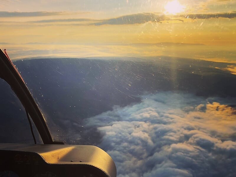 Vue depuis le cockpit d'un hélicoptère au-dessus d'une mer de nuages au coucher du soleil.