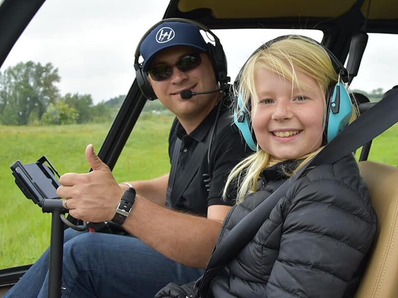 Un pilote d’hélicoptère souriant et une jeune passagère, tous deux portant des casques audio.