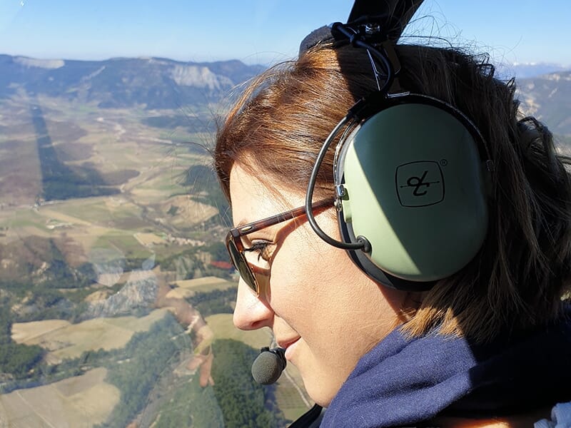 Vue latérale d'une passagère dans un hélicoptère, contemplant un paysage montagneux à travers la fenêtre.