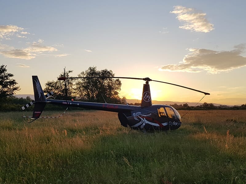 Hélicoptère noir posé dans un champ, illuminé par un coucher de soleil.