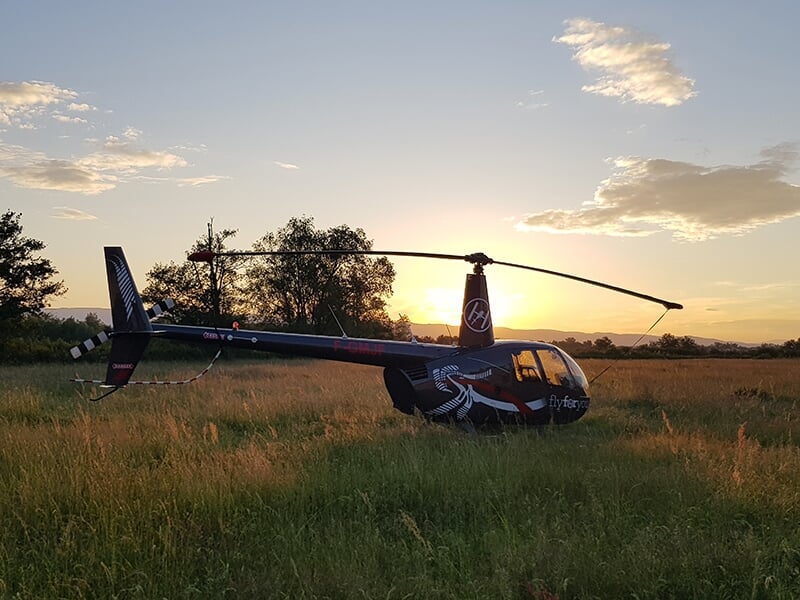 Hélicoptère noir posé dans un champ, illuminé par un coucher de soleil.