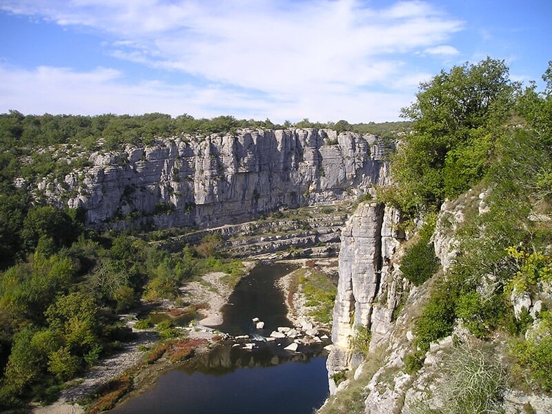 Gorges avec falaises calcaires, rivière sinueuse et végétation dense sous un ciel bleu parsemé de nuages.