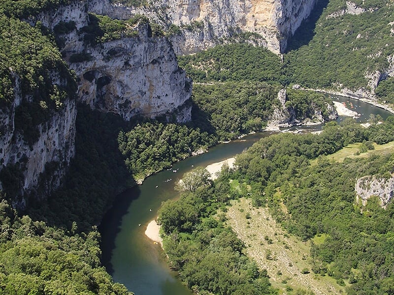 Vue aérienne d'une rivière sinueuse bordée de falaises rocheuses et de forêts verdoyantes.