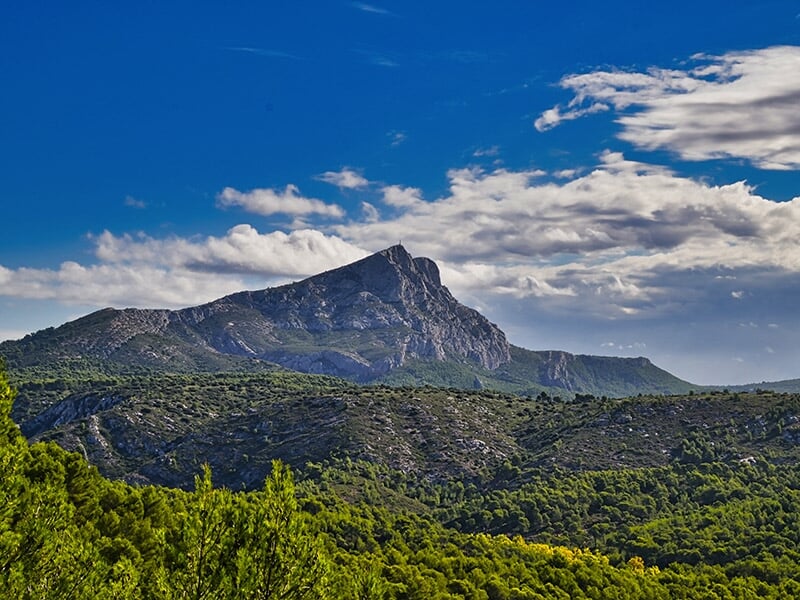 Majestueuse montagne Sainte-Victoire sous un ciel bleu vif, entourée d'une végétation luxuriante.