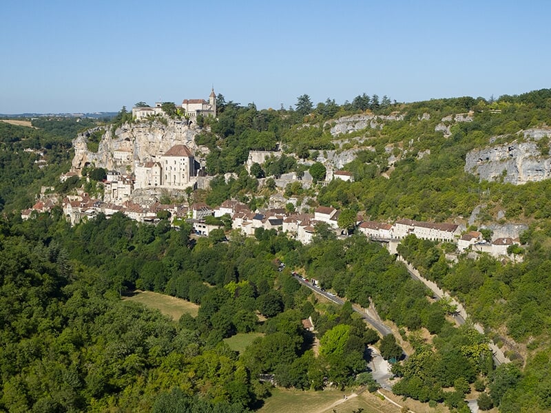 Vue panoramique de Rocamadour, un village pittoresque niché sur une falaise, entouré de forêts verdoyantes et de paysages vallonné