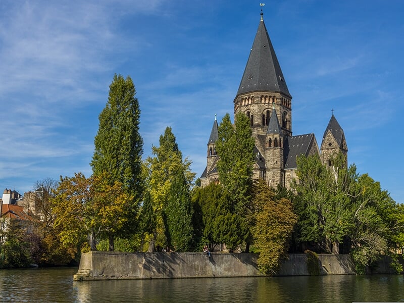 Vue panoramique d'une cathédrale gothique derrière un lac entouré de végétation et de bâtiments historiques.