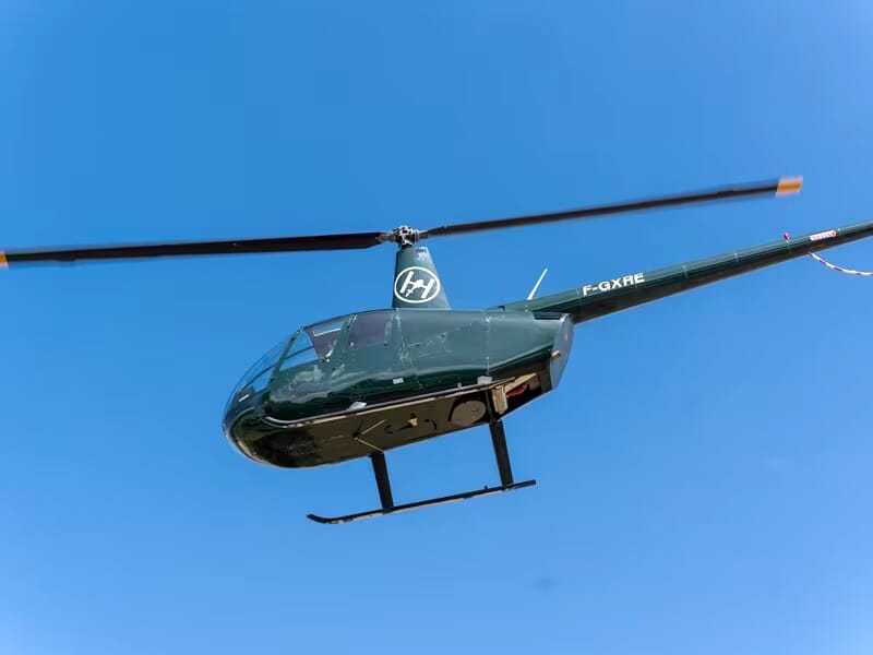 Hélicoptère vert volant dans un ciel bleu clair, pris en photo depuis le sol, vue latérale nette et détaillée.