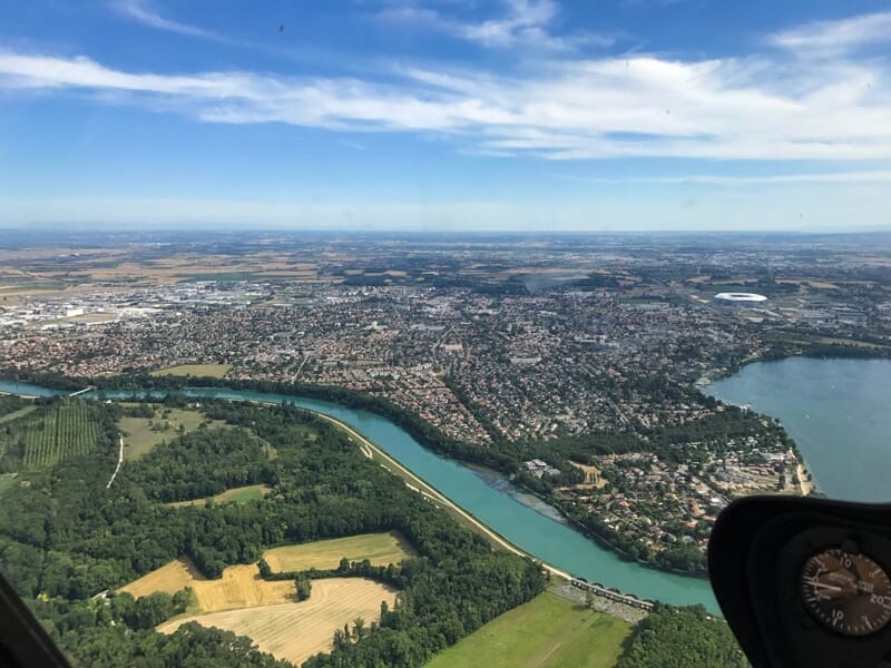 Vue aérienne d'une ville avec rivière et campagne sous un ciel partiellement nuageux prise depuis un hélicoptère.
