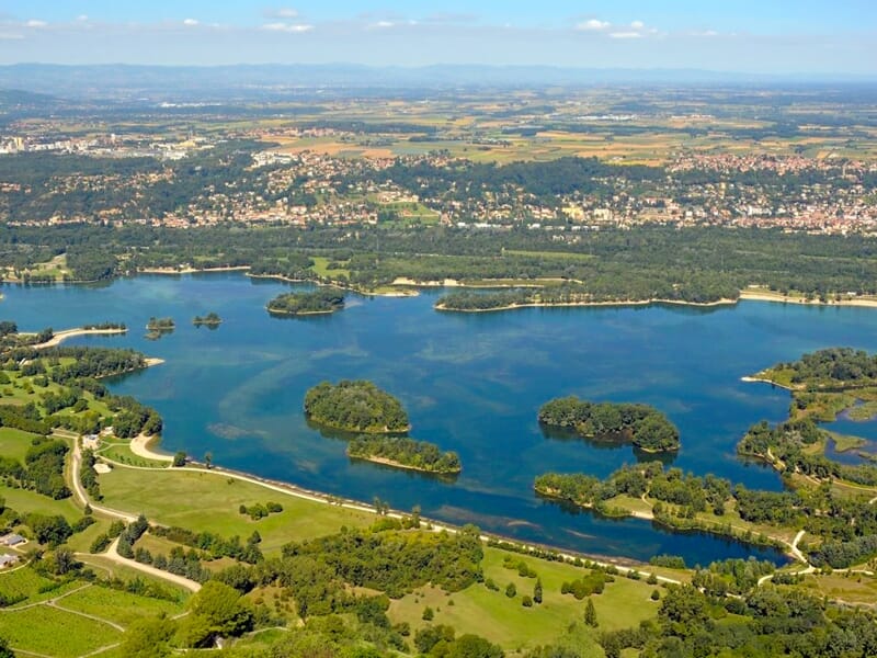 Paysage vu du ciel montrant un grand lac avec plusieurs îles et une forêt dense autour par une journée ensoleillée.