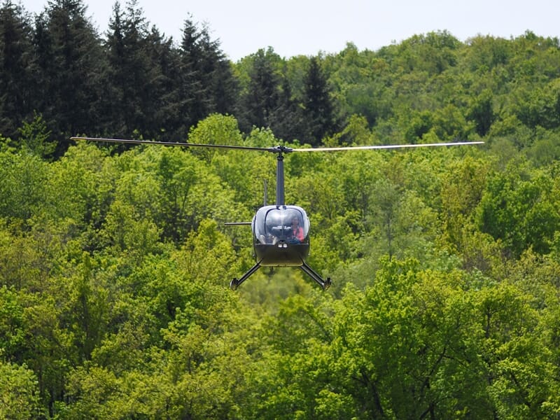 Hélicoptère volant au-dessus d'une forêt dense avec des arbres verts sous un ciel clair et lumineux.