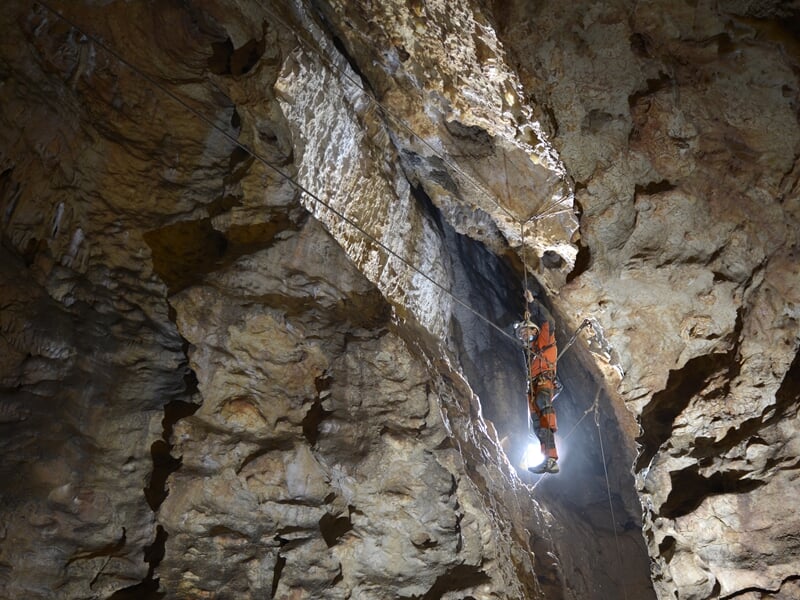 Spéléologue équipé d'un casque et lampe explore une étroite cavité rocheuse éclairée dans une grotte.